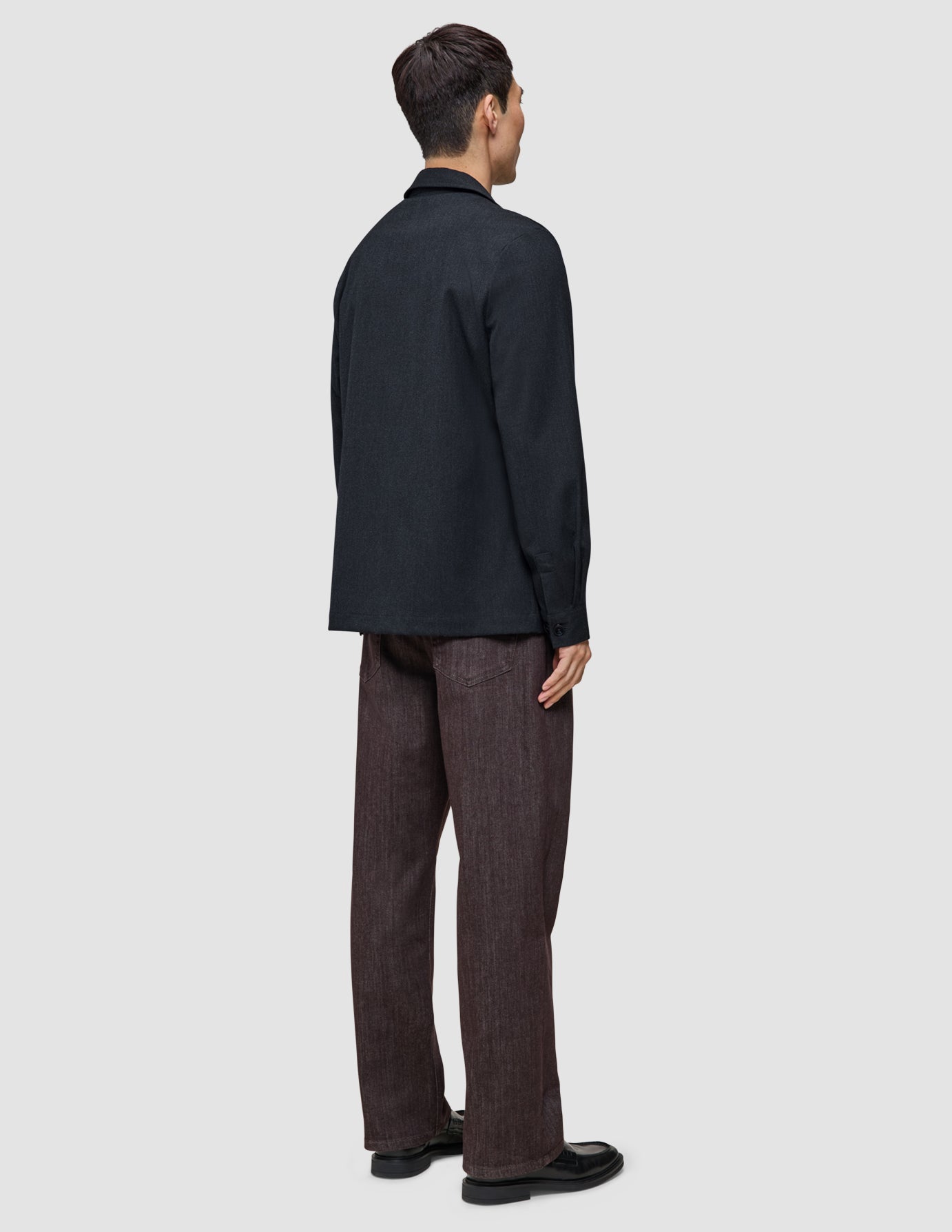 En man sedd bakifrån, klädd i en mörkblå Atelier-överskjorta, mörka byxor och svarta loafers.